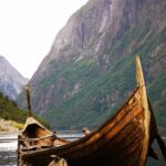 Νορβηγία. Μία παλιά ξύλινη βάρκα στο βάθος του φιόρδ ενώ ο Βίκινγκ στέκει αγέρωχ