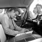 Ο Τζέιμς Ντιν κάθεται σε ένα αυτοκίνητο, υπογράφοντας φωτογραφίες για τους θαυμαστές του στο απόγειο της φροντίδας του...